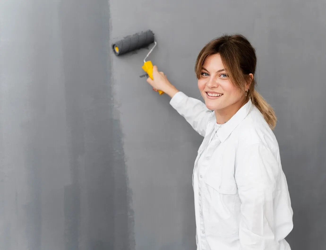 Plano medio de una mujer sonriente pintando una pared.